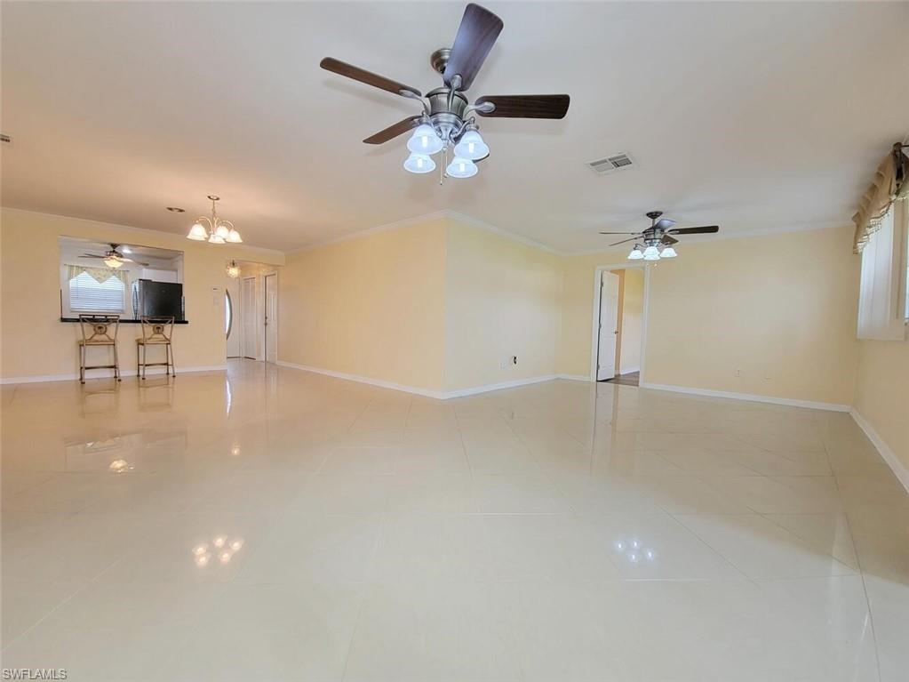 Unfurnished living room with ceiling fan, crown molding, a chandelier, and light tile patterned floors
