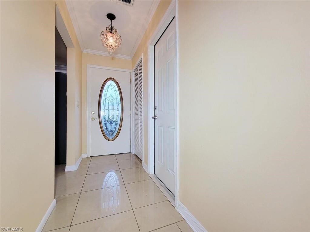 Doorway to outside featuring tile patterned floors, a chandelier, and crown molding