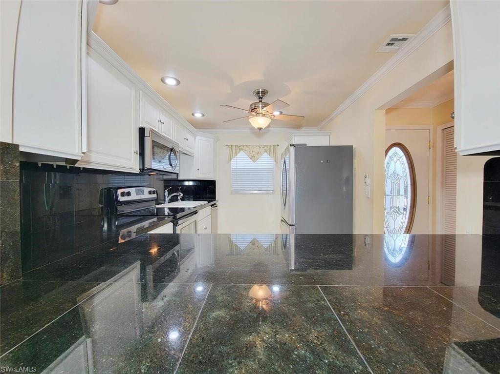Kitchen with stainless steel appliances, white cabinets, backsplash, ornamental molding, and recessed lighting