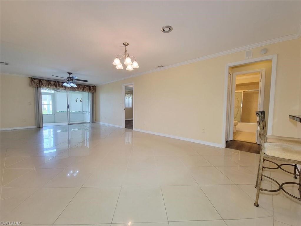 Empty room with ornamental molding, a ceiling fan, a chandelier, and light tile patterned floors