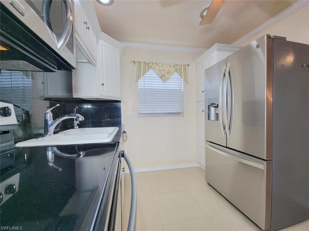Kitchen featuring appliances with stainless steel finishes, decorative backsplash, white cabinetry, light tile patterned floors, and crown molding