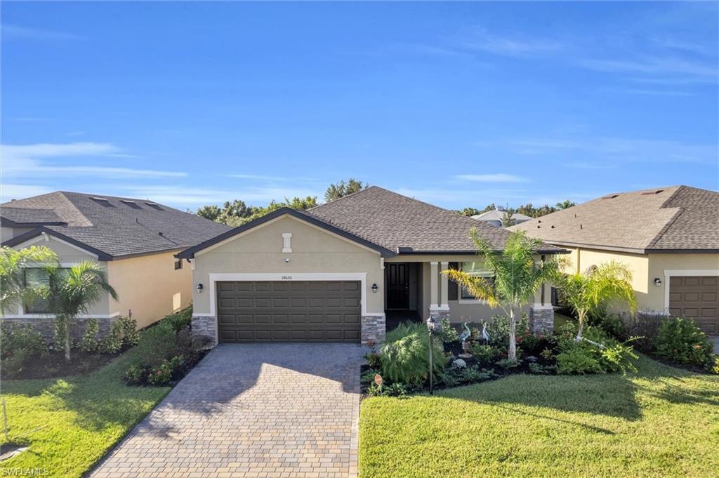 Single story home featuring stucco siding, stone siding, decorative driveway, an attached garage, and a front yard