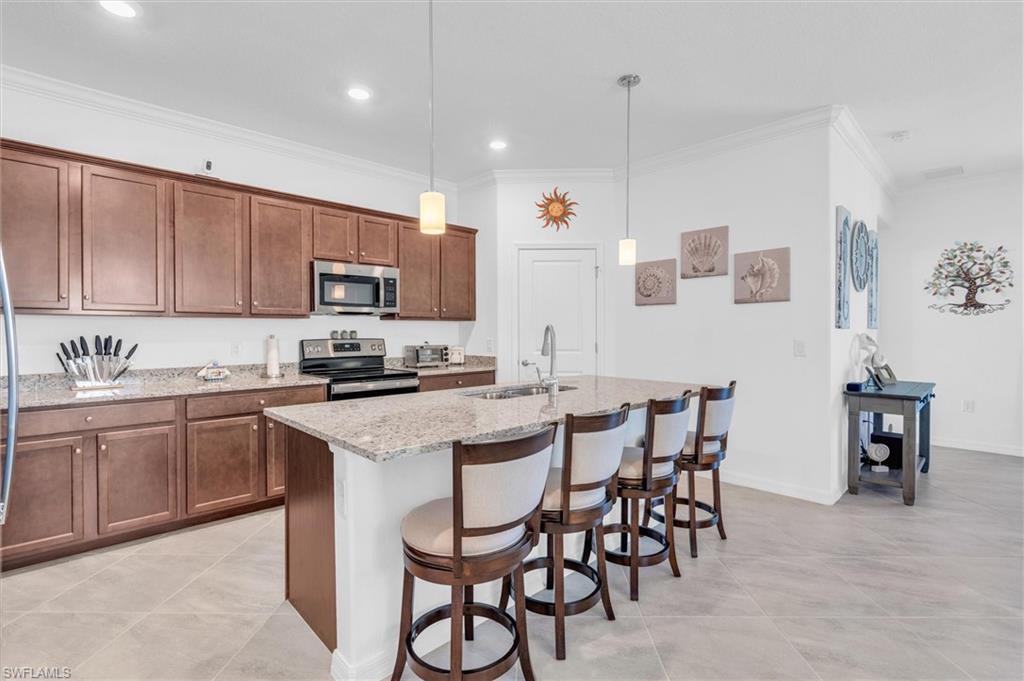 Kitchen with a breakfast bar, crown molding, hanging light fixtures, appliances with stainless steel finishes, and light stone countertops
