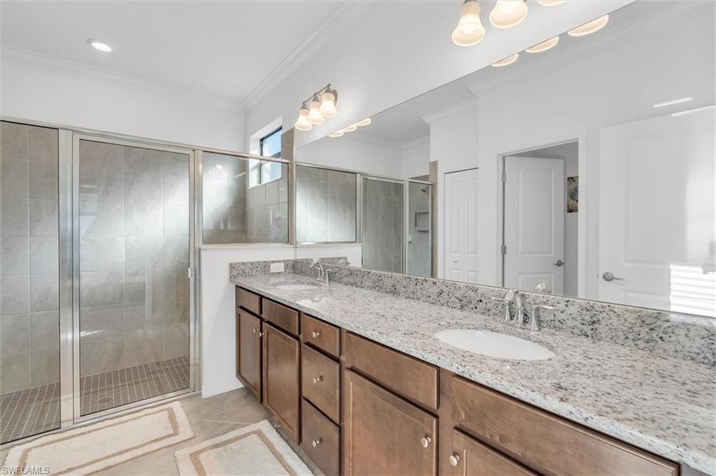 Full bathroom featuring a shower stall, double vanity, crown molding, and light tile patterned flooring