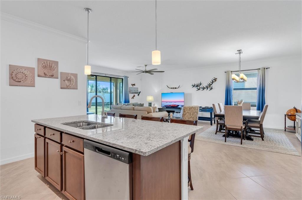 Kitchen with decorative light fixtures, stainless steel dishwasher, ceiling fan, light stone countertops, and ornamental molding