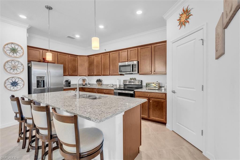 Kitchen with brown cabinetry, crown molding, pendant lighting, a breakfast bar area, and stainless steel appliances