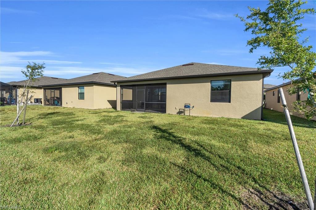 Back of property featuring a lawn, stucco siding, a sunroom, and roof with shingles