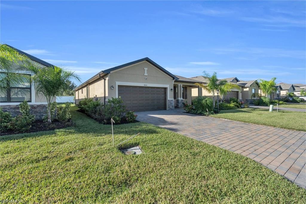 Ranch-style house featuring stucco siding, stone siding, decorative driveway, an attached garage, and a front yard