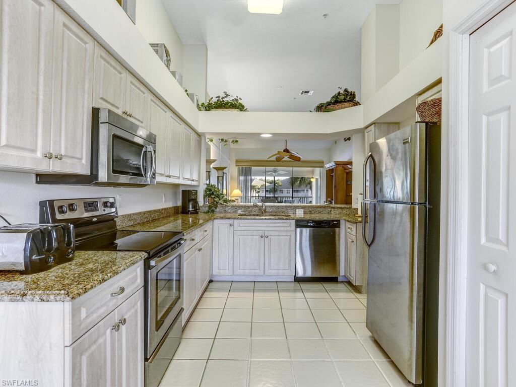 Kitchen featuring stainless steel appliances, dark stone countertops, light tile patterned floors, a towering ceiling, and white cabinetry