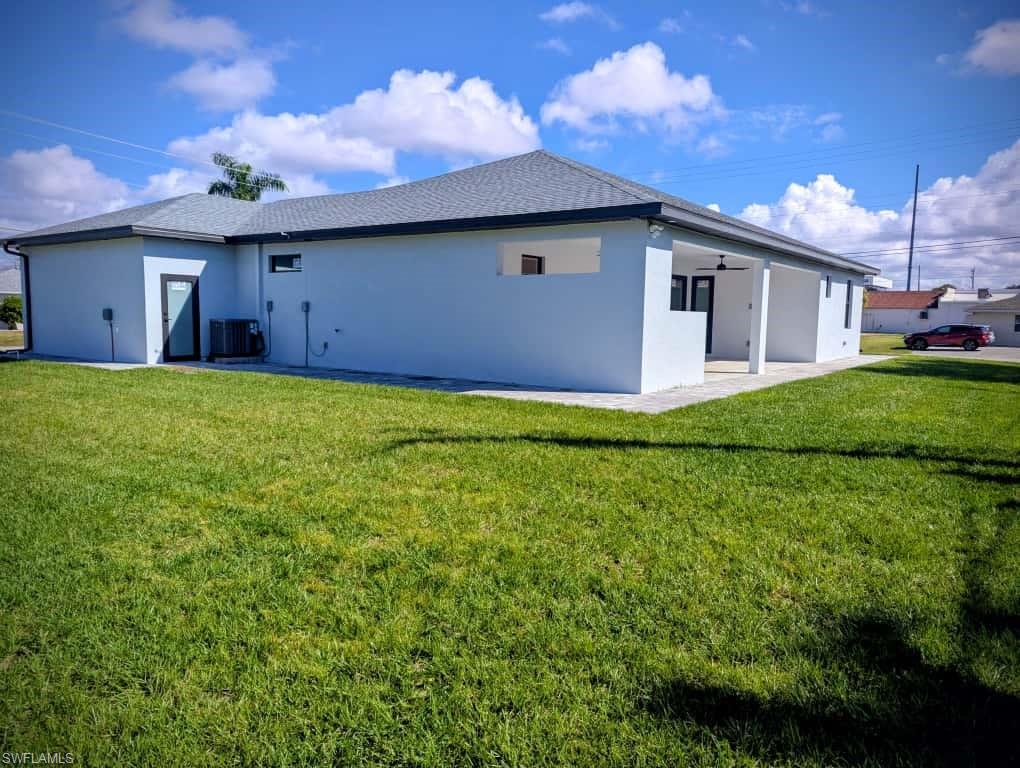 Rear view of property featuring a yard, stucco siding, and roof with shingles