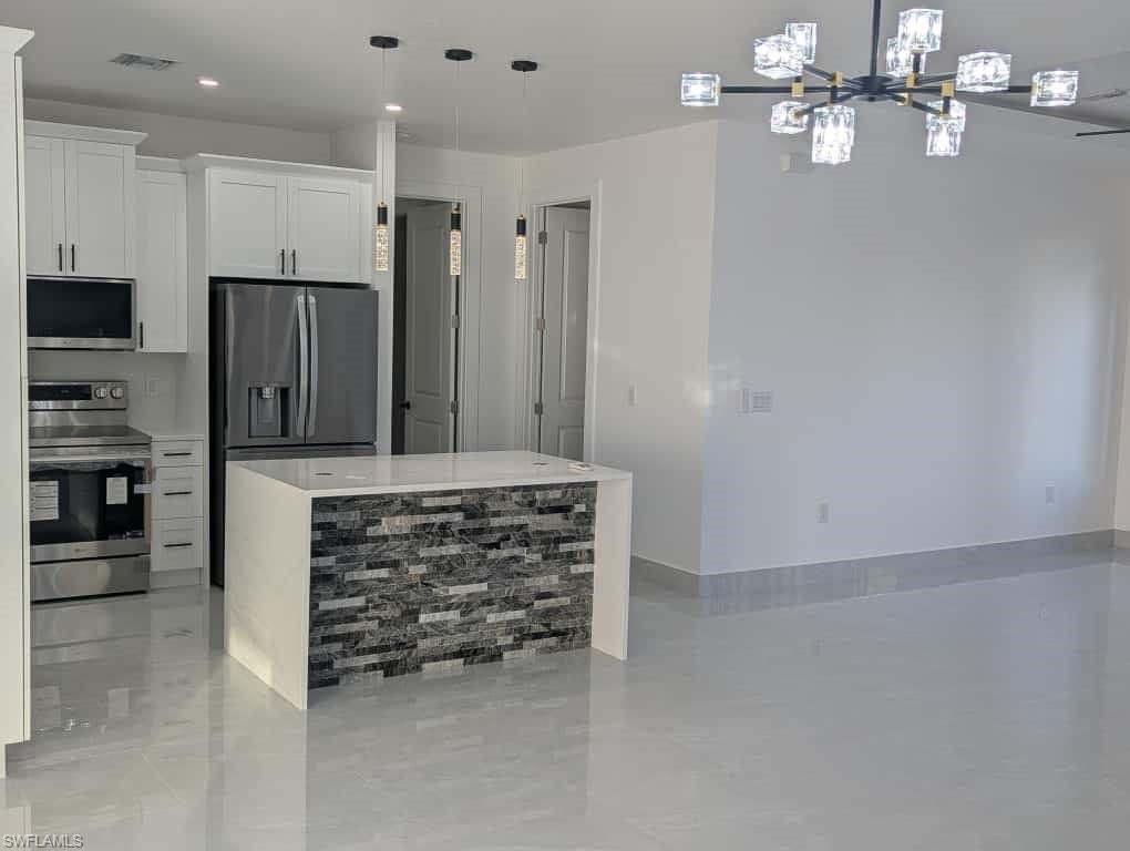 Kitchen featuring stainless steel appliances, decorative light fixtures, white cabinets, a chandelier, and light stone counters