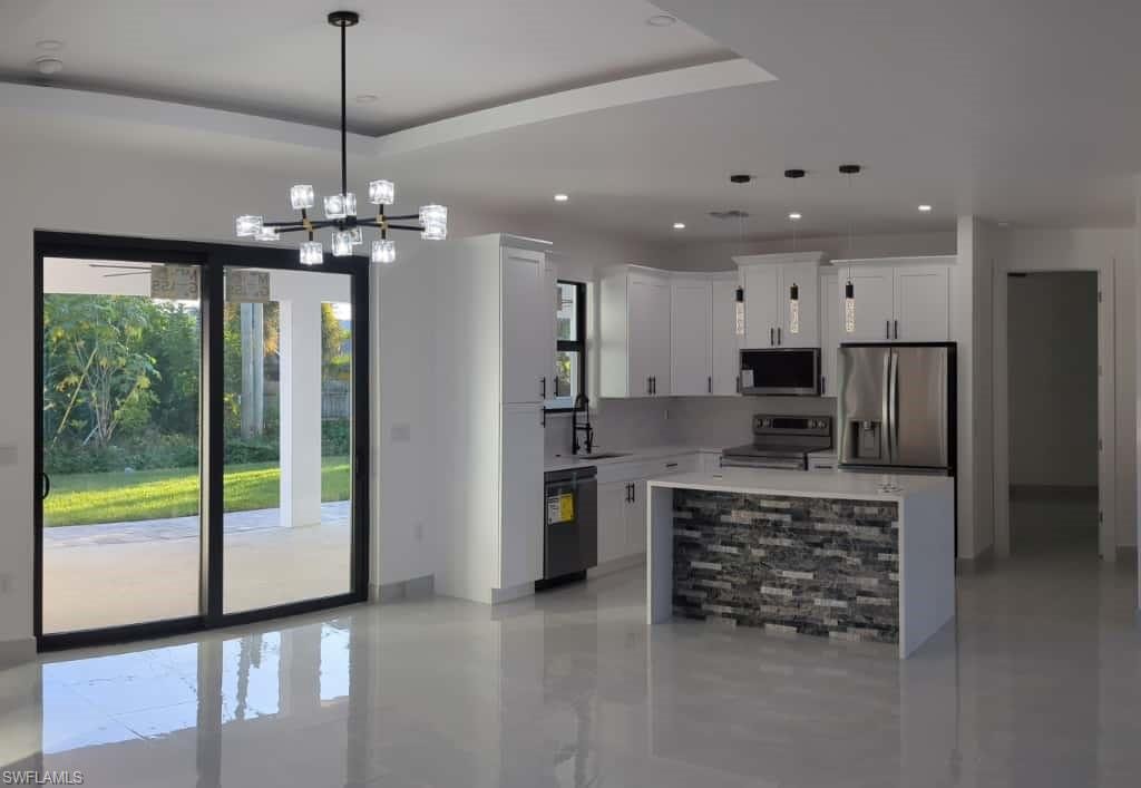 Kitchen with hanging light fixtures, appliances with stainless steel finishes, white cabinetry, a center island, and a tray ceiling