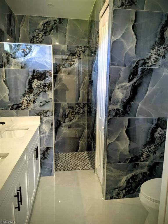 Full bathroom featuring double vanity, a marble finish shower, tile walls, and light tile patterned floors