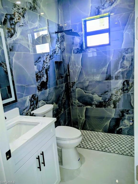 Bathroom with tile walls, vanity, a marble finish shower, and tile patterned flooring