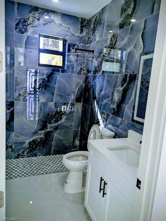 Bathroom featuring tile walls, vanity, a marble finish shower, and tile patterned floors