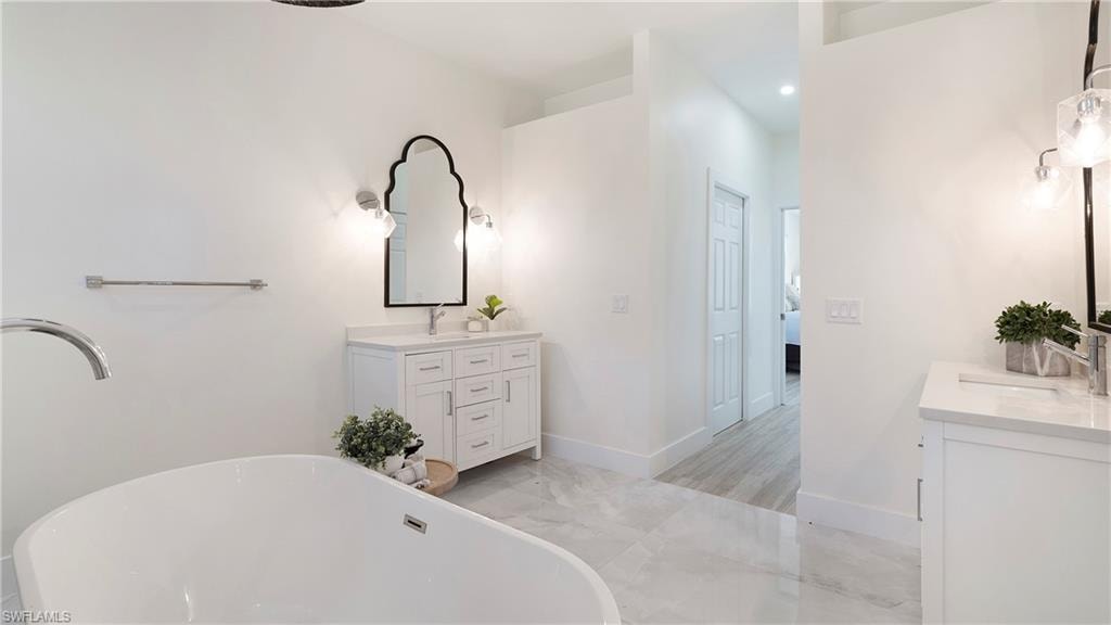 Full bathroom with a freestanding tub, light marble finish floors, and two vanities