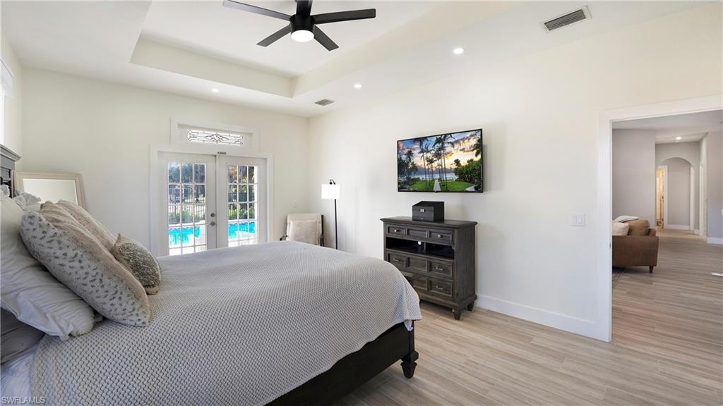 Bedroom featuring french doors, arched walkways, light wood-style floors, access to exterior, and a ceiling fan