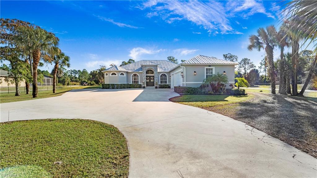 Mediterranean / spanish-style home with driveway, stucco siding, a front lawn, stone siding, and a metal roof