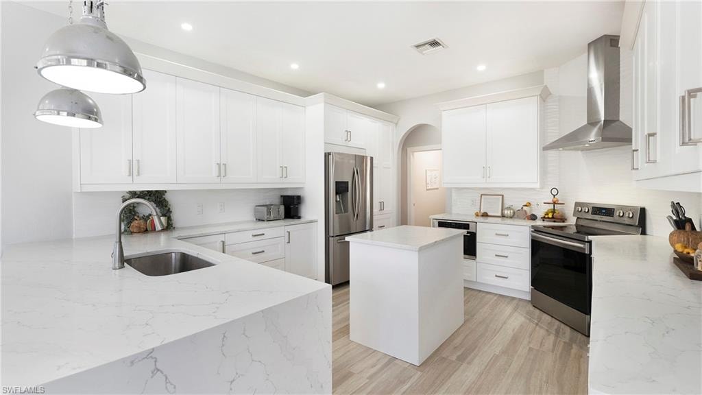 Kitchen with a kitchen island, stainless steel appliances, wall chimney exhaust hood, pendant lighting, and white cabinets