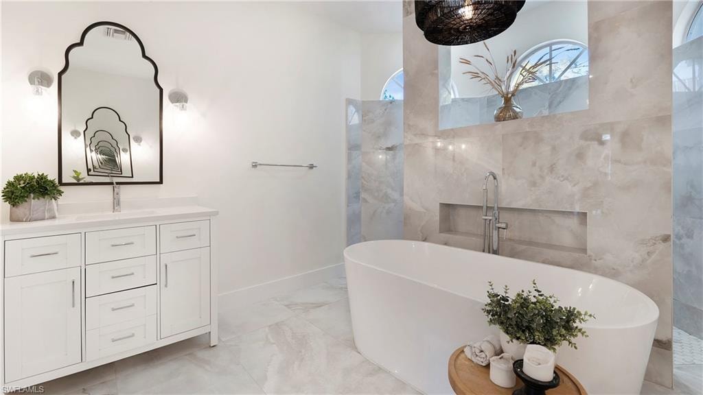 Bathroom featuring light marble finish flooring, vanity, and a freestanding tub