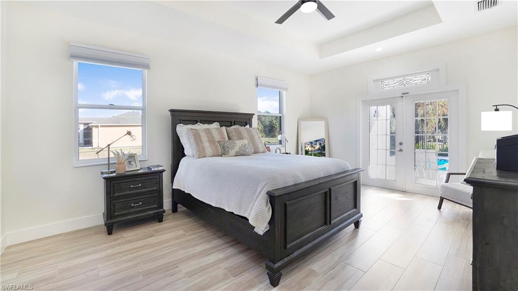 Bedroom featuring french doors, light wood finished floors, access to outside, ceiling fan, and a tray ceiling