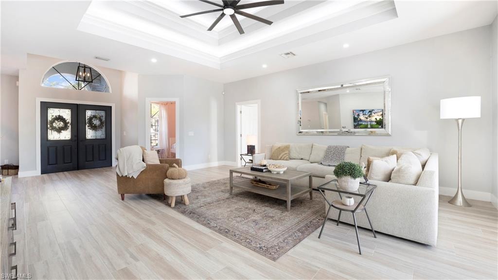 Living area with light wood-type flooring, a raised ceiling, ceiling fan, and recessed lighting