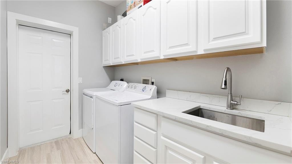 Laundry room featuring washing machine and dryer, cabinet space, and light wood finished floors
