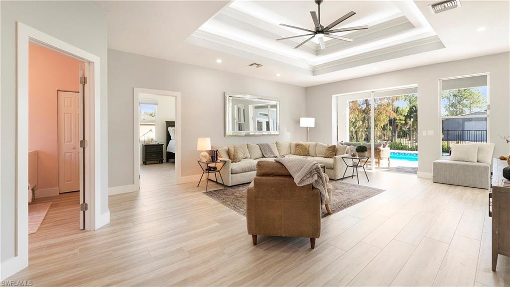 Living room featuring ornamental molding, a ceiling fan, light wood finished floors, recessed lighting, and a raised ceiling