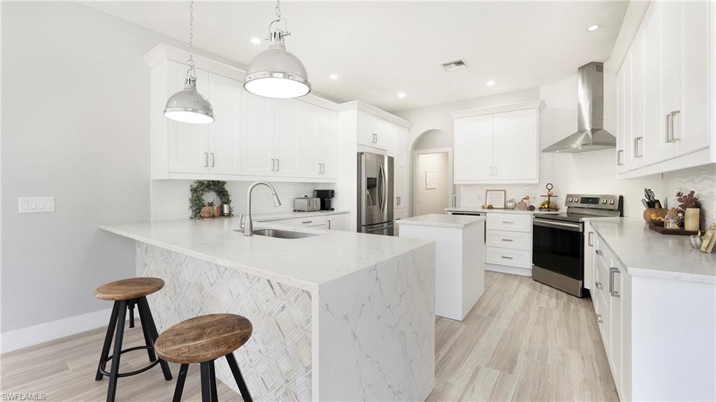 Kitchen with a center island, a kitchen bar, appliances with stainless steel finishes, wall chimney range hood, and a peninsula