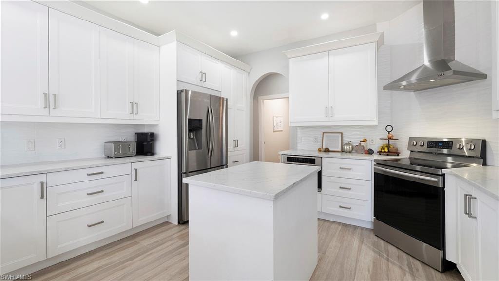 Kitchen featuring stainless steel appliances, wall chimney range hood, decorative backsplash, a center island, and white cabinetry