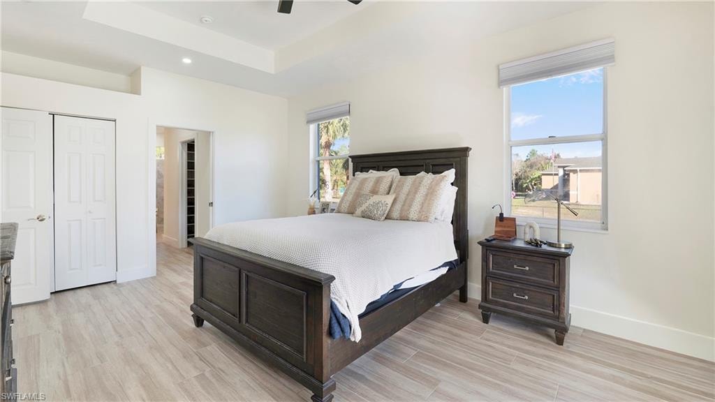 Bedroom with wood tiled floors, a tray ceiling, a closet, a ceiling fan, and recessed lighting