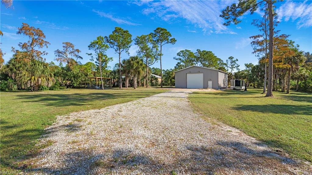 View of green lawn featuring a garage, gravel driveway, and an outbuilding