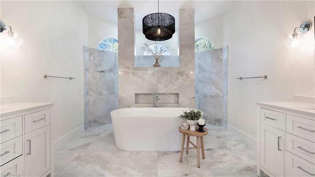 Bathroom featuring vanity, a soaking tub, light marble finish floors, and plenty of natural light