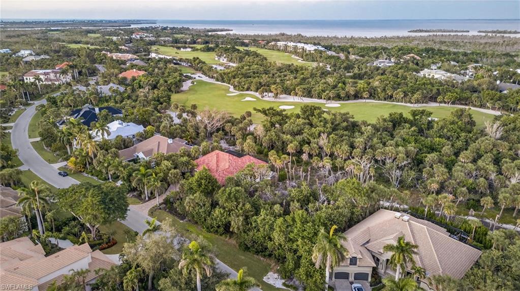 Aerial view of property and surrounding area featuring a golf course, a large body of water, and nearby suburban area