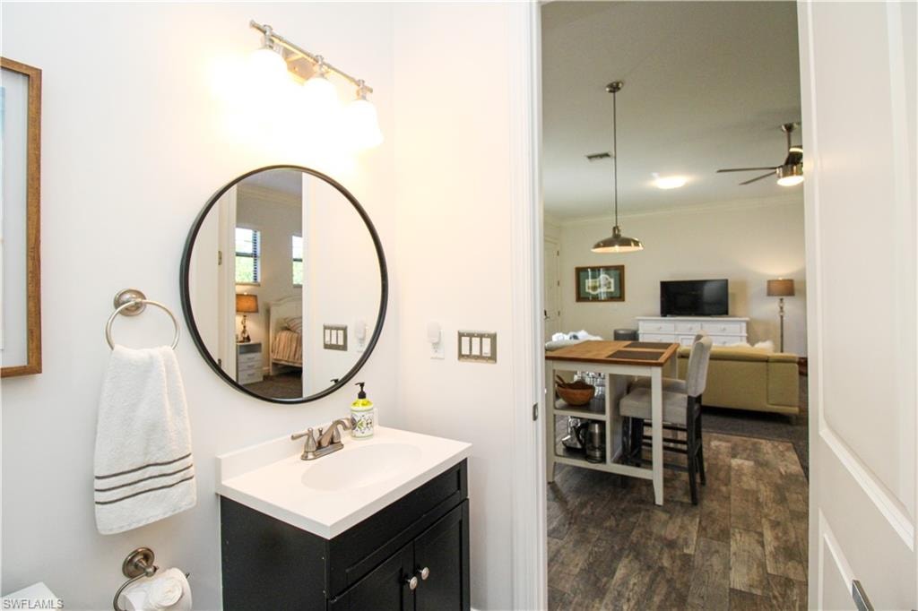 Bathroom featuring hardwood / wood-style floors, ceiling fan, ornamental molding, and vanity