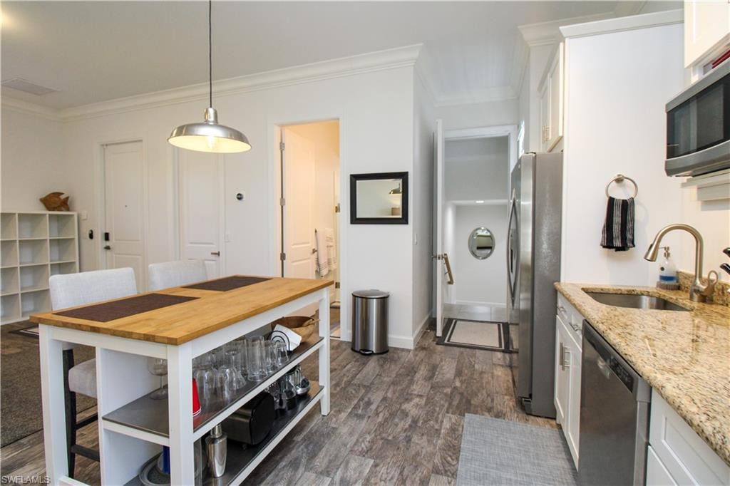 Kitchen featuring appliances with stainless steel finishes, light stone counters, dark wood-type flooring, sink, and white cabinetry