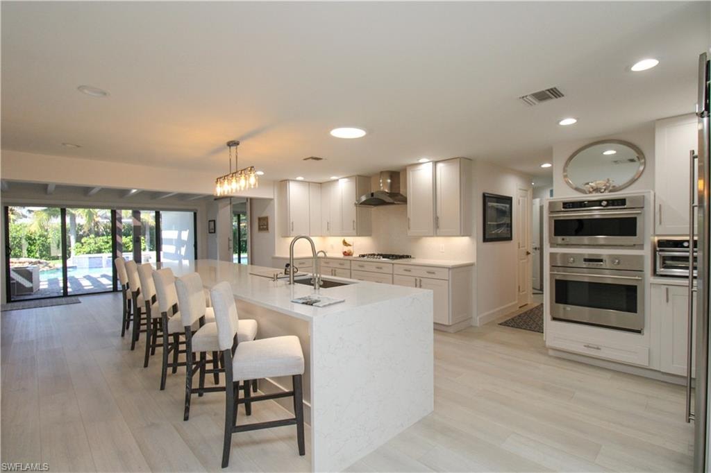 Kitchen with sink, wall chimney range hood, gas cooktop, decorative light fixtures, and a kitchen island with sink