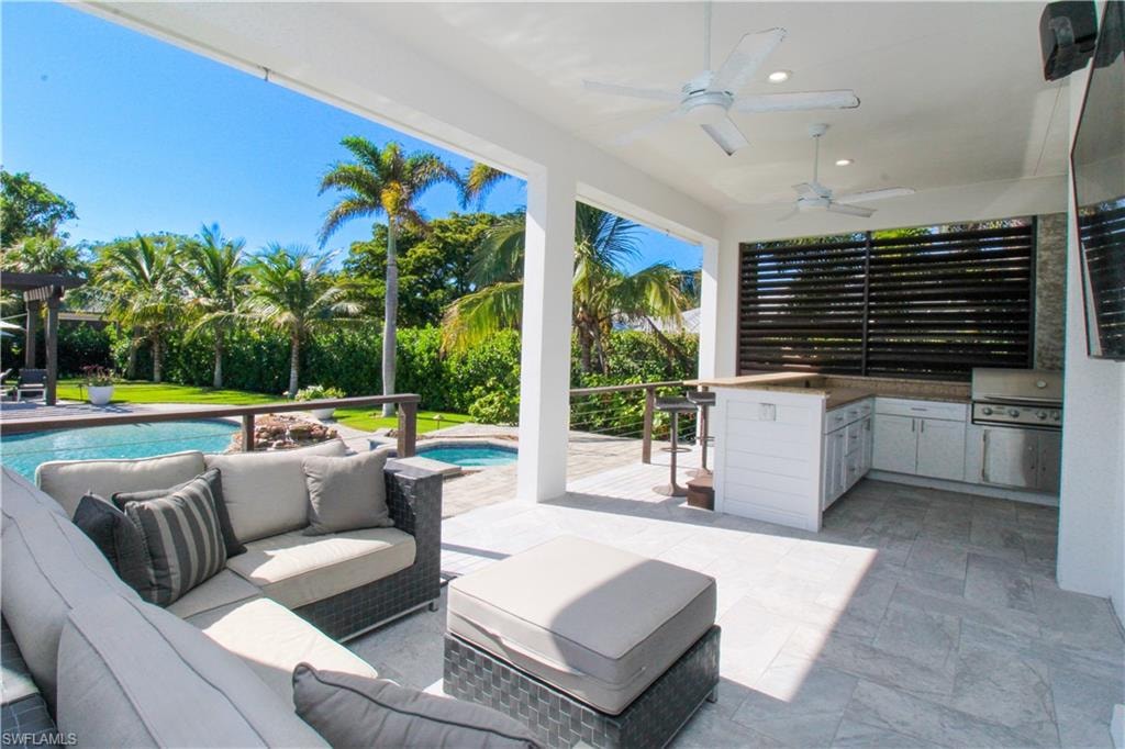 View of patio featuring outdoor lounge area, ceiling fan, exterior kitchen, a hot tub, and area for grilling