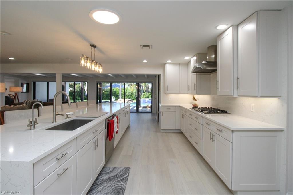 Kitchen featuring white cabinets, pendant lighting, sink, and wall chimney range hood