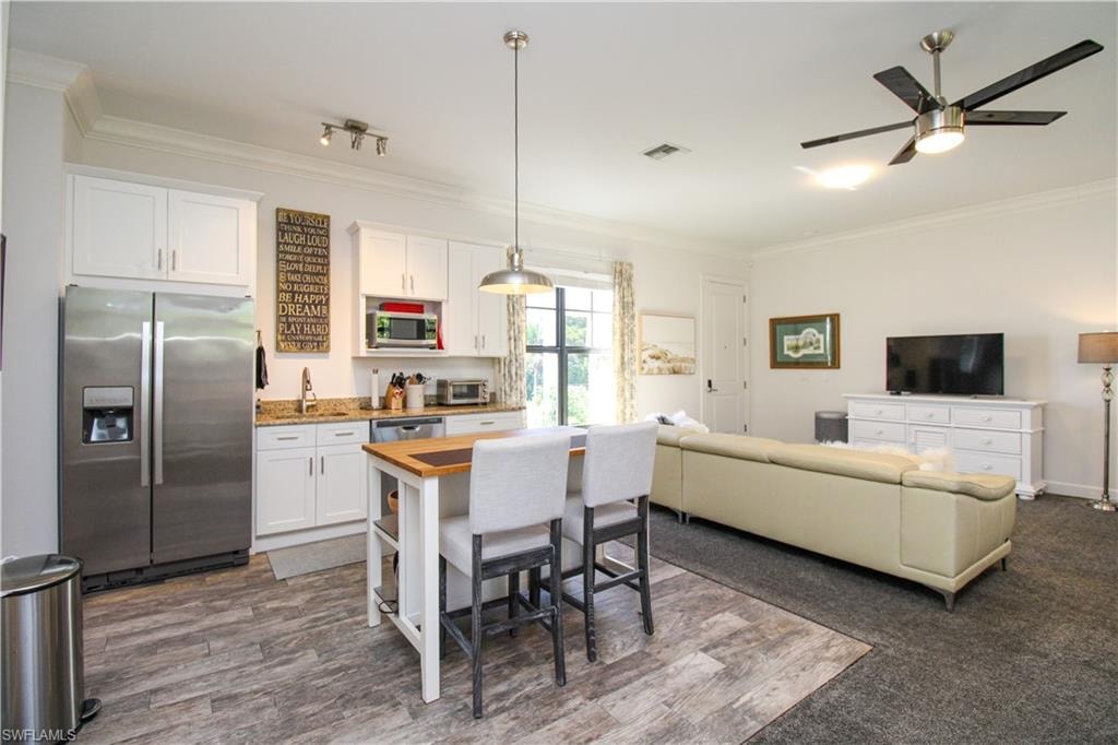 Kitchen with wood counters, appliances with stainless steel finishes, crown molding, pendant lighting, and white cabinets