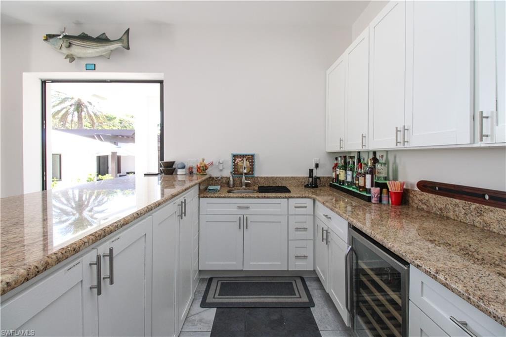 Kitchen with light stone countertops, dark tile patterned flooring, white cabinetry, and beverage cooler