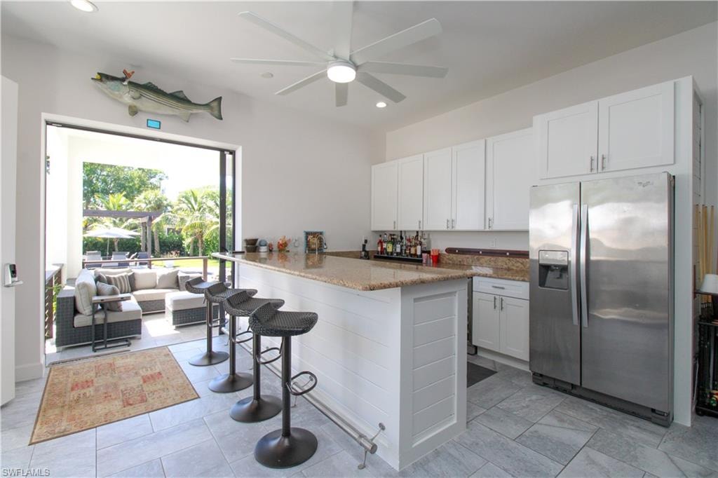 Kitchen with stone counters, stainless steel fridge with ice dispenser, kitchen peninsula, a breakfast bar, and white cabinets