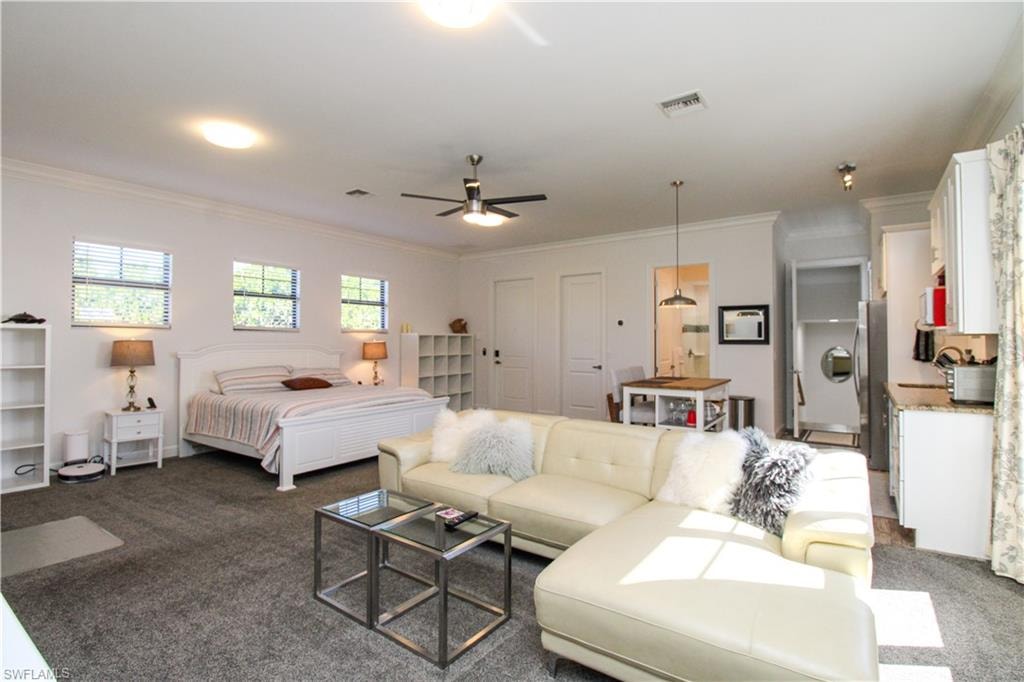 Carpeted bedroom featuring ceiling fan, crown molding, and stainless steel refrigerator