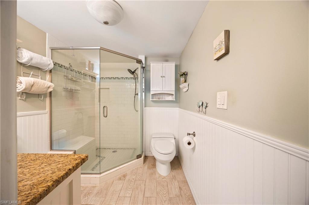 Bathroom with hardwood / wood-style floors, toilet, and a shower with shower door