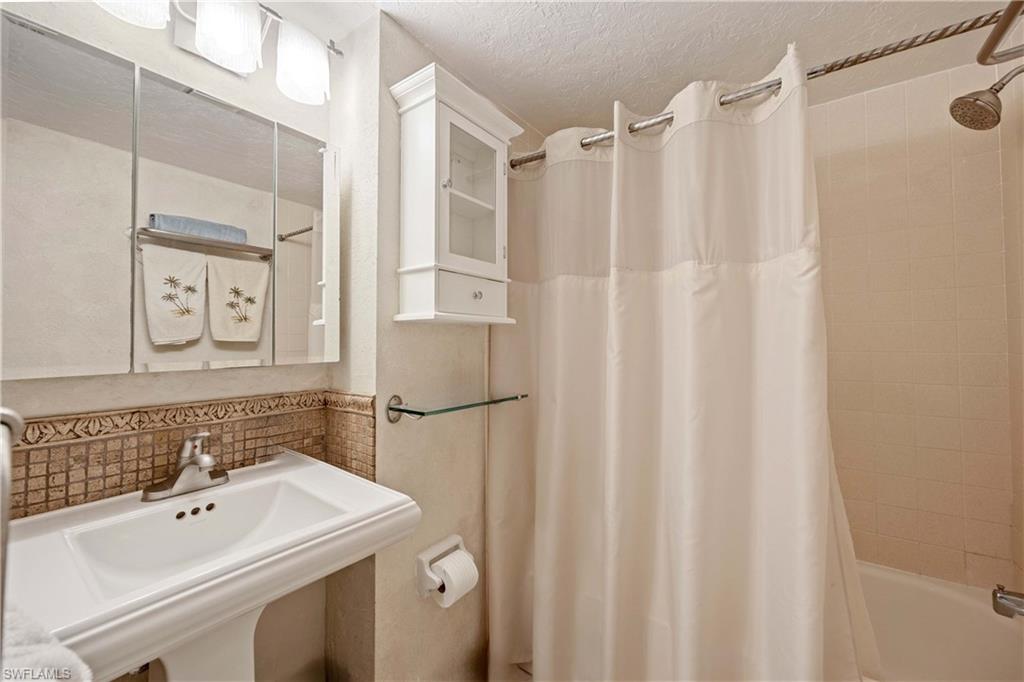 Bathroom featuring decorative backsplash, sink, shower / bath combination with curtain, and a textured ceiling