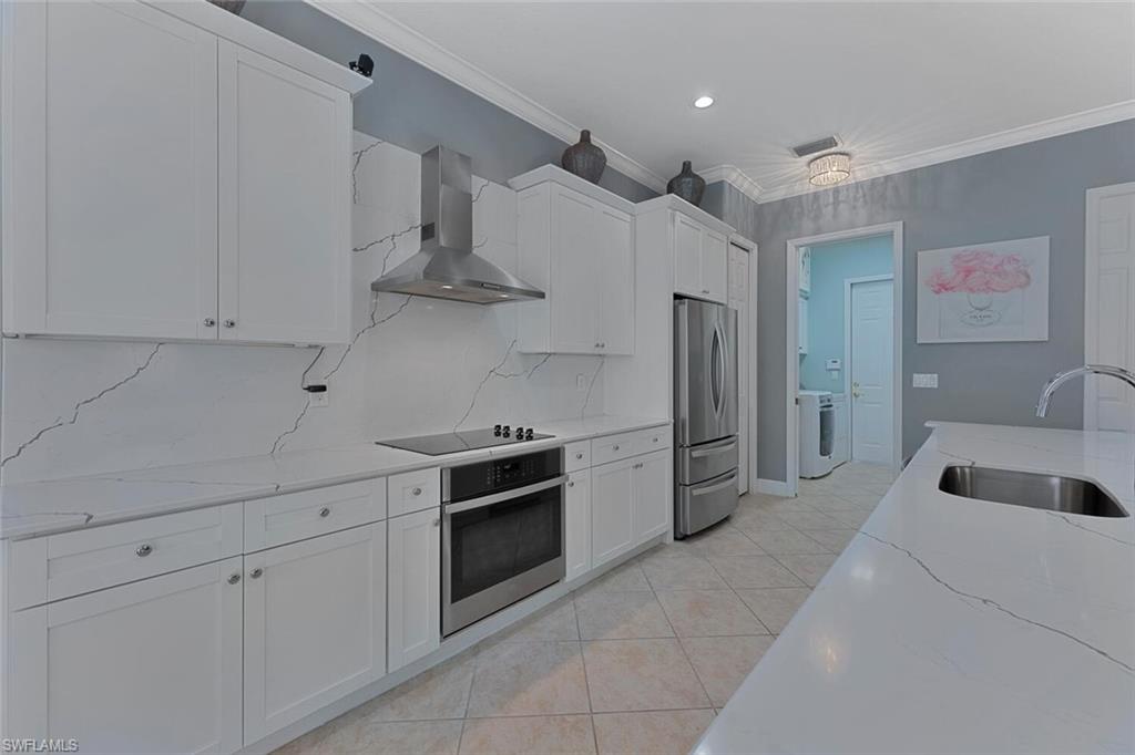 Kitchen with wall chimney range hood, ornamental molding, washer / dryer, stainless steel appliances, and a sink