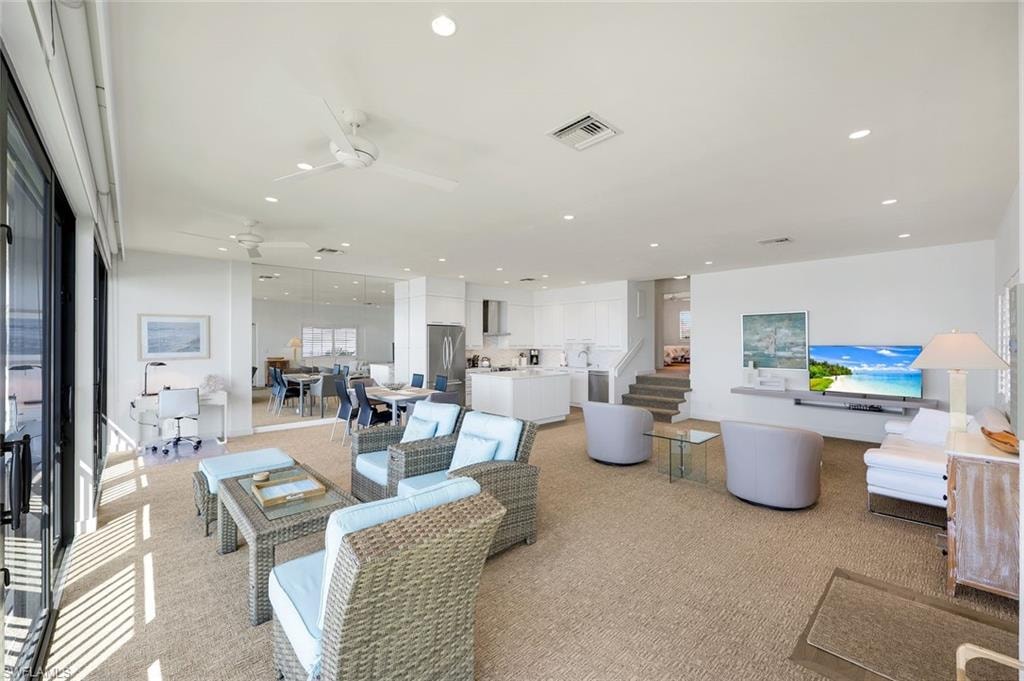 Living room featuring stairs, ceiling fan, recessed lighting, and light colored carpet