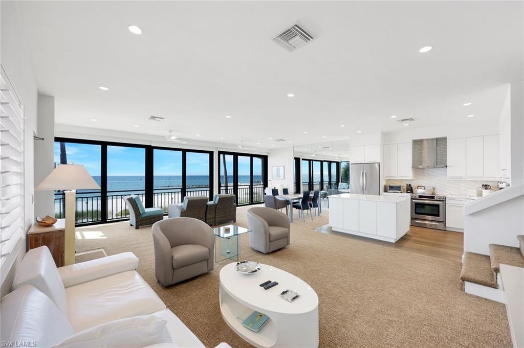 Living area featuring a water view, stairs, recessed lighting, expansive windows, and light carpet