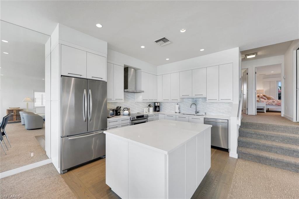 Kitchen featuring stainless steel appliances, white cabinetry, light colored carpet, a center island, and recessed lighting