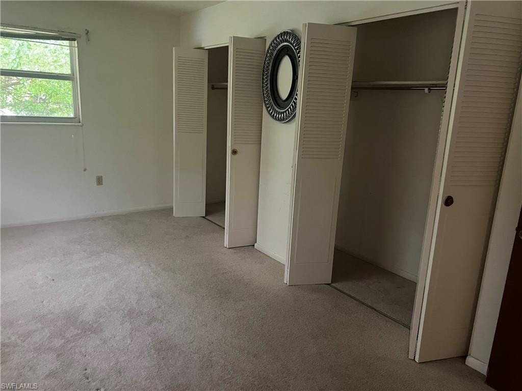 Unfurnished bedroom featuring light carpet and two closets